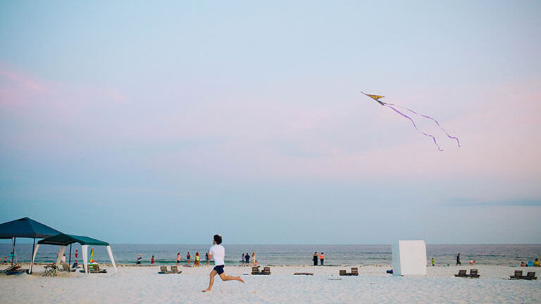 Boy running on a beach with a kite at sunset