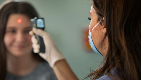 Dr wearing mask taking young woman's temperature