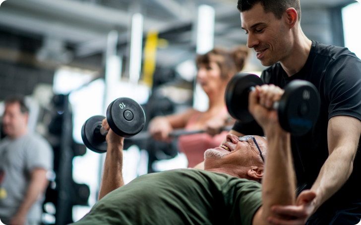 Man spotting another man lifting dumbells in gym