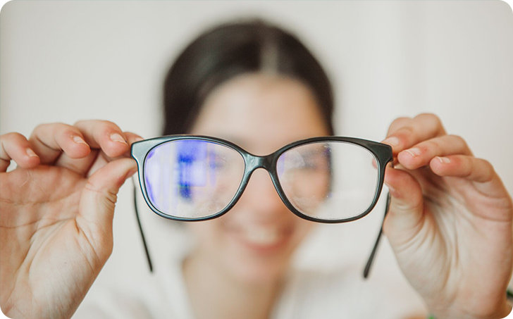 Woman holding pair of spectacles in front of face