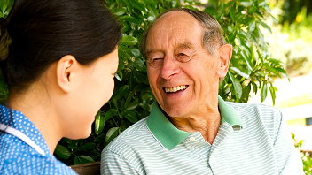 A care worker smiling with an older person outdoors.
