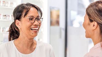 A person trying on glasses in a store, assisted by a staff member.
