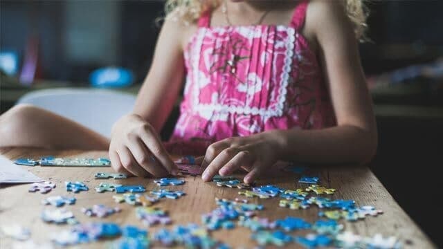 A child assembles a jigsaw puzzle atop a wooden table.