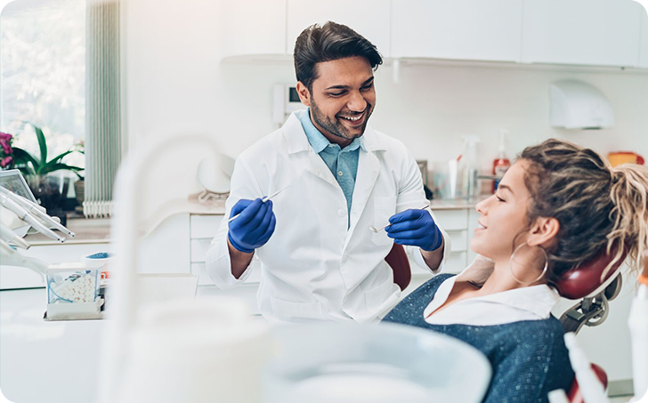 Male dentist smiling whilst working on female patient